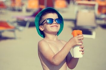 ילד בחוף הים עם כובע משקפי שמש ובקבוק מים
